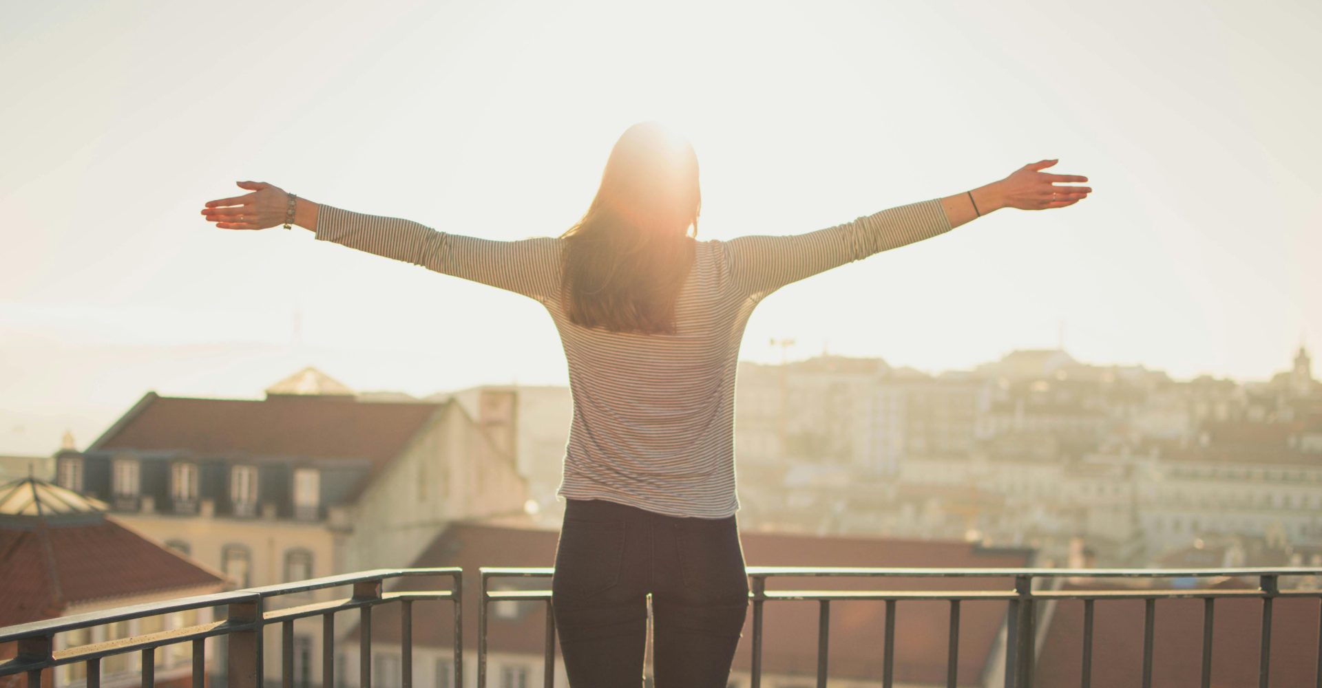 Woman on balcony embracing morning sunlight.