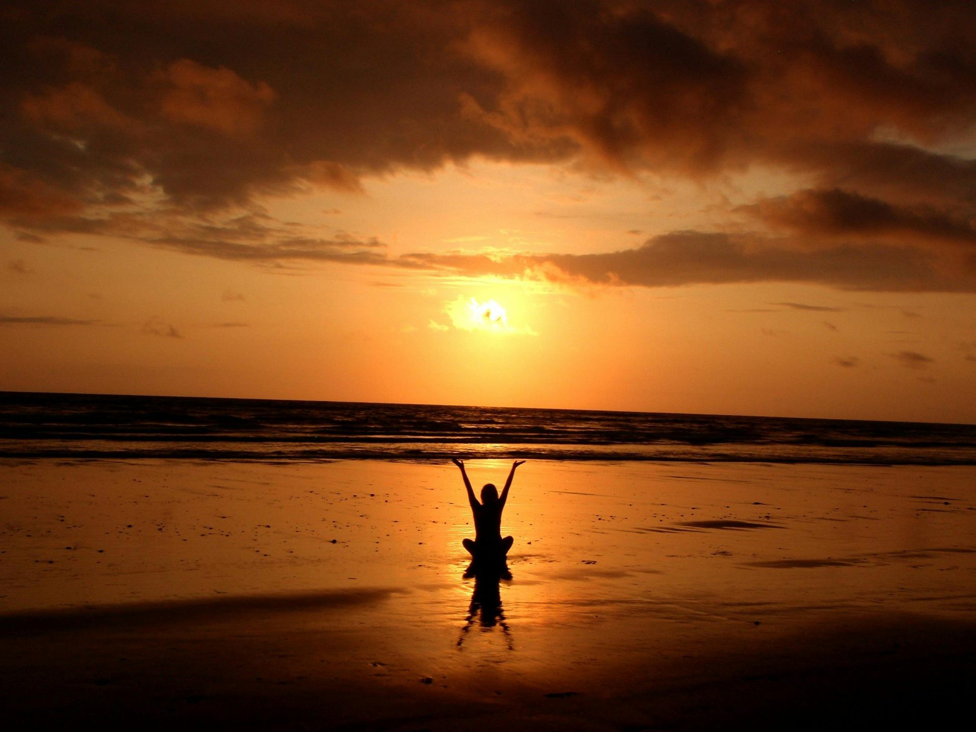 Silhouette on beach celebrating sunset’s golden glow.