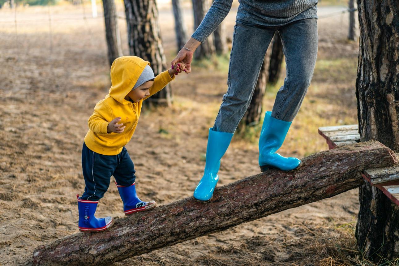 Child in yellow hoodie balancing with adult's help.