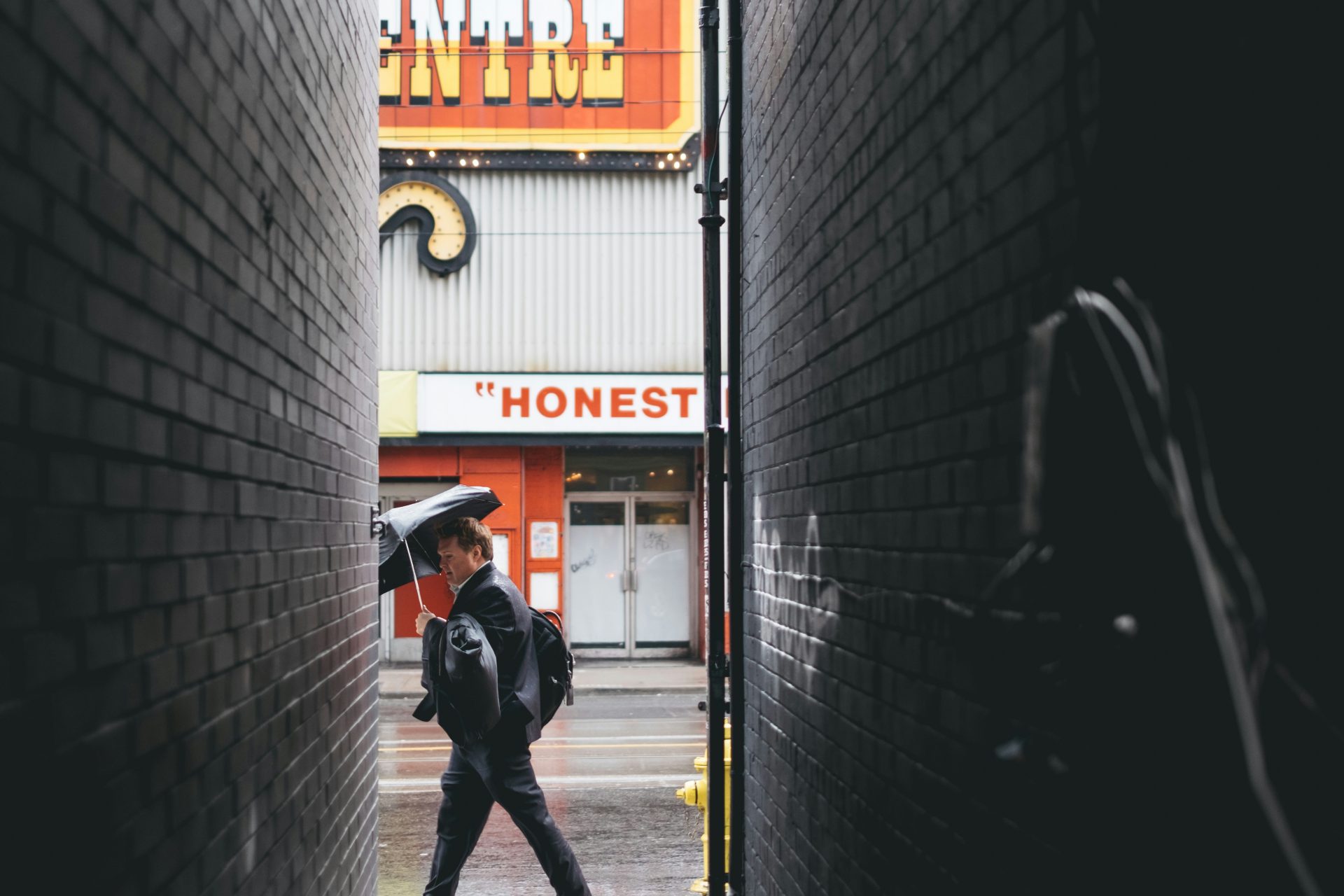 Man walking in alley holding an umbrella.